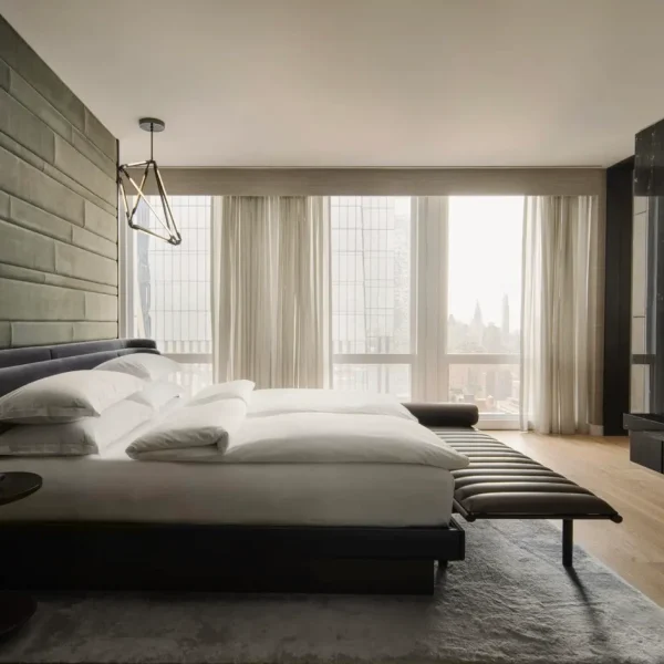Modern hotel room with low platform bed, floor‑to‑ceiling windows, and minimalist neutral decor.