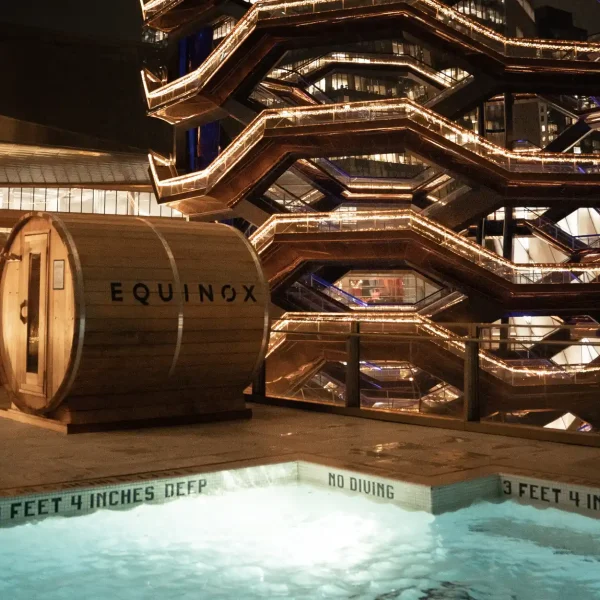 Night rooftop with glowing hot tub and EQUINOX sauna beside the lit Vessel structure.