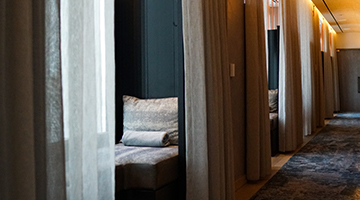 Dim hallway with floor-length curtains, alcove benches, and rolled towels creating a calm spa atmosphere.