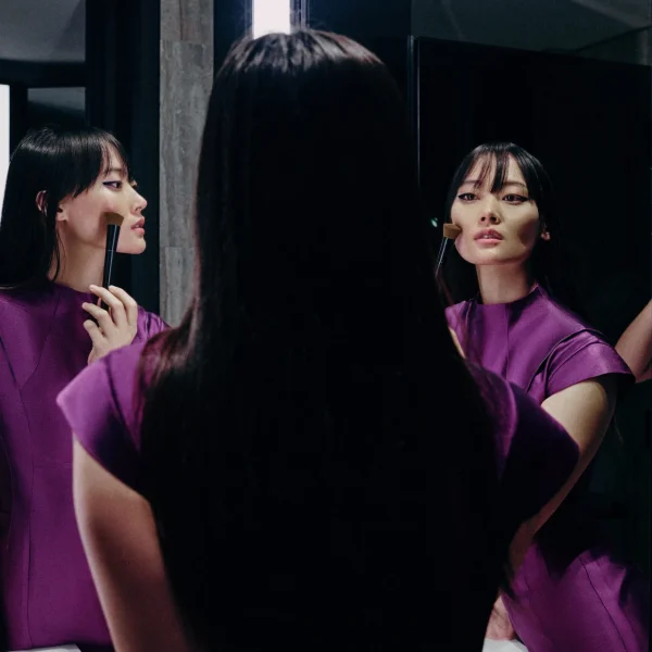 Woman in purple outfit applies makeup before mirror, her reflection creating cinematic modern dressing.