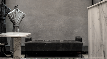 Minimalist space with a low gray sofa, marble table, draped coat stands, and ribbed partition.