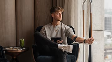 Man in lounge chair by a city window using a tablet with a wellness IV drip.