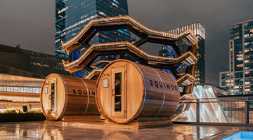 Two Equinox sauna pods on a rooftop at night with pool reflections and a honeycomb structure.
