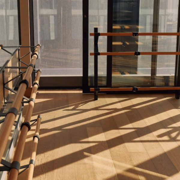 Bright studio with wooden floors, tall windows, and parallel ballet barres in natural light.