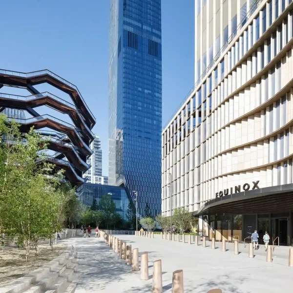 Modern plaza with EQUINOX façade on one side and the Vessel on the other under a clear sky.