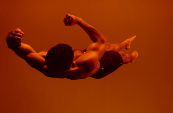 Athletic man appears to be flying midair in orange light, fists clenched.