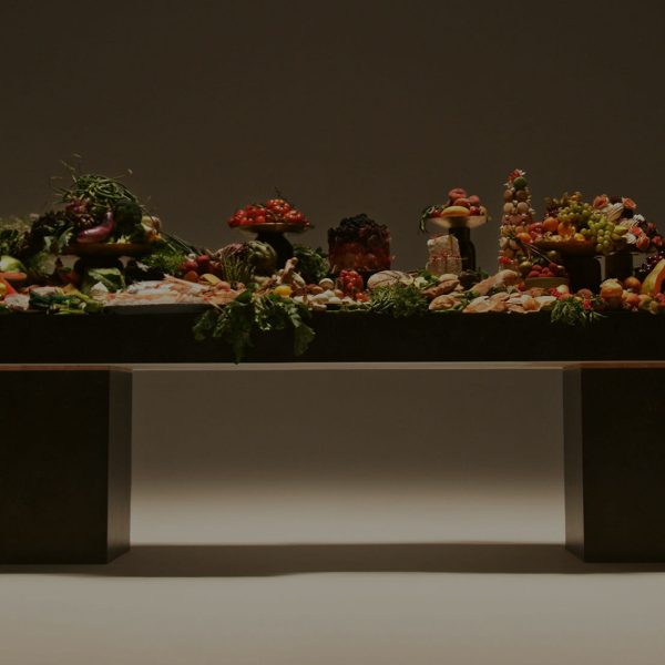 Table loaded with fruits vegetables breads cheeses arranged beautifully under soft dramatic lights.