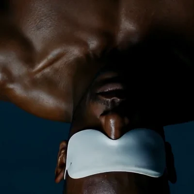 Upside-down close-up of shirtless muscular individual wearing white eye mask, with dramatic lighting and artistic contrast