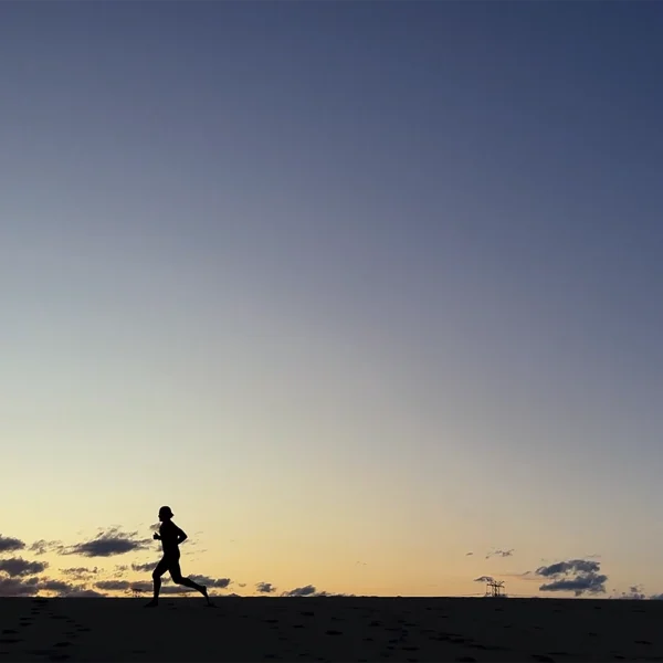 Silhouette of person running at sunrise with orange and blue sky and distant power line structure