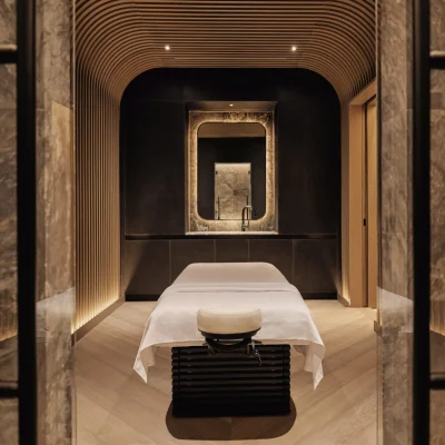 Luxurious spa room with massage table, curved wood slats, stone-framed mirror, and soft ambient lighting