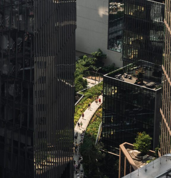 Elevated urban walkway with greenery surrounded by glass buildings and pedestrians in modern cityscape
