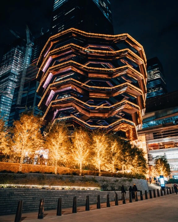 The Vessel lit up at night with festive lights and golden trees in Hudson Yards, NYC