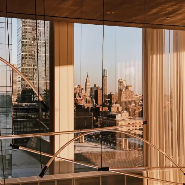 City skyline at golden hour seen through floor-to-ceiling windows with sheer curtains and sculptural light fixture