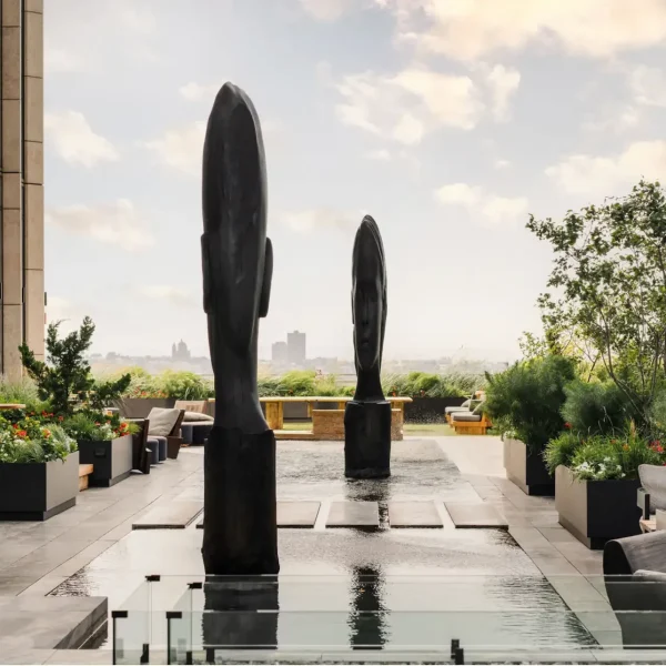 Equinox rooftop terrace with twin head sculptures in reflecting pool, lounge seating, greenery, and city view