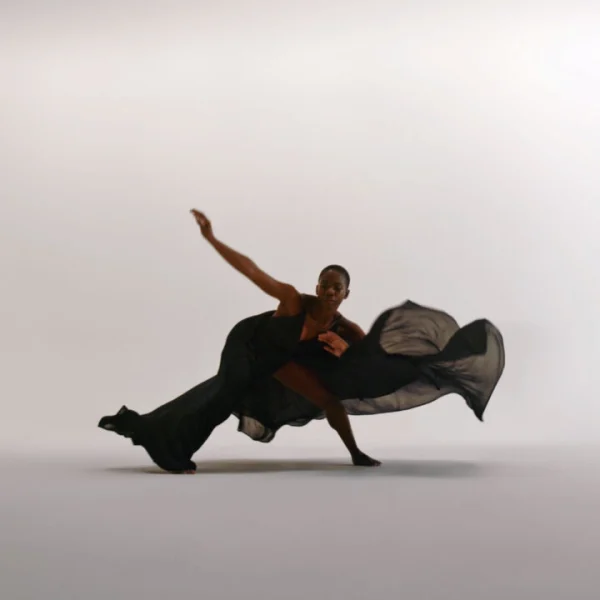 Dancer in flowing black outfit mid-motion against light backdrop, expressing strength and grace