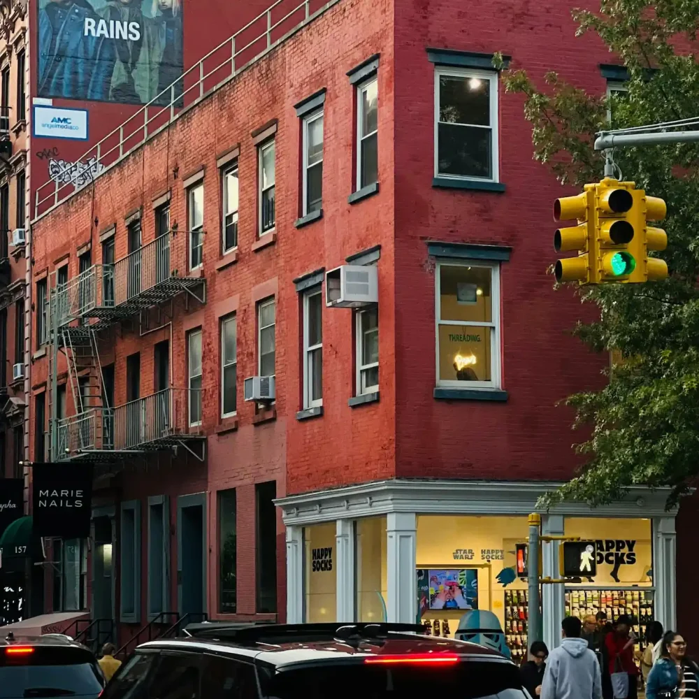 Urban street corner with red brick building, Happy Socks storefront, and pedestrians under AMC billboard