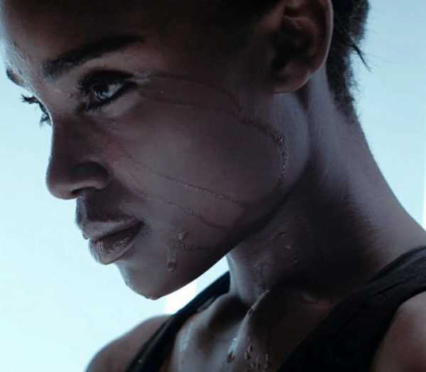 Side profile of person with water streaming down face and neck in cool-toned wellness studio setting