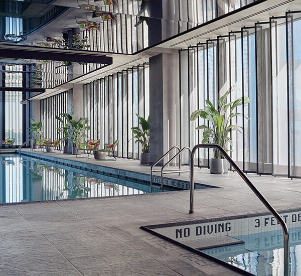 Indoor pool with floor-to-ceiling windows, lounge chairs, potted plants, and reflective ceiling panels