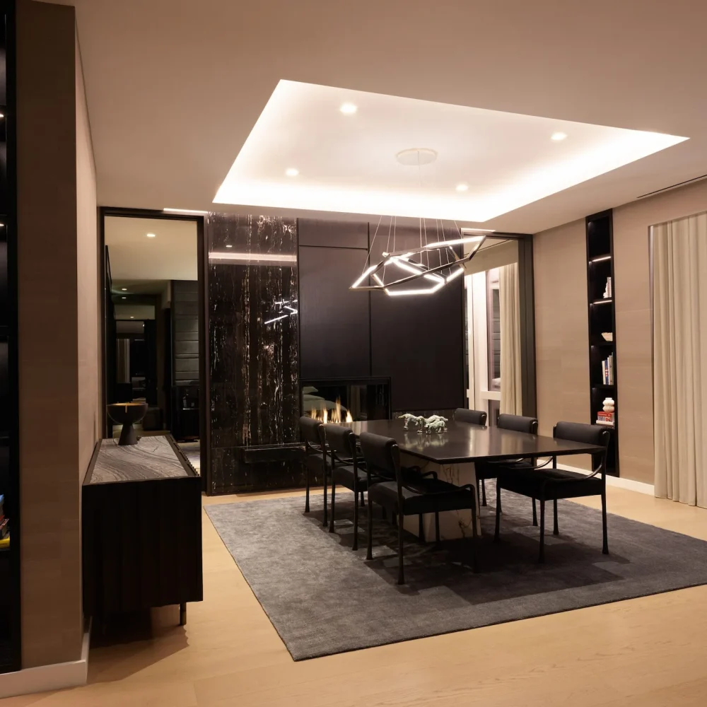 Modern dining room with black table, geometric chandelier, marble fireplace wall, and built-in shelves