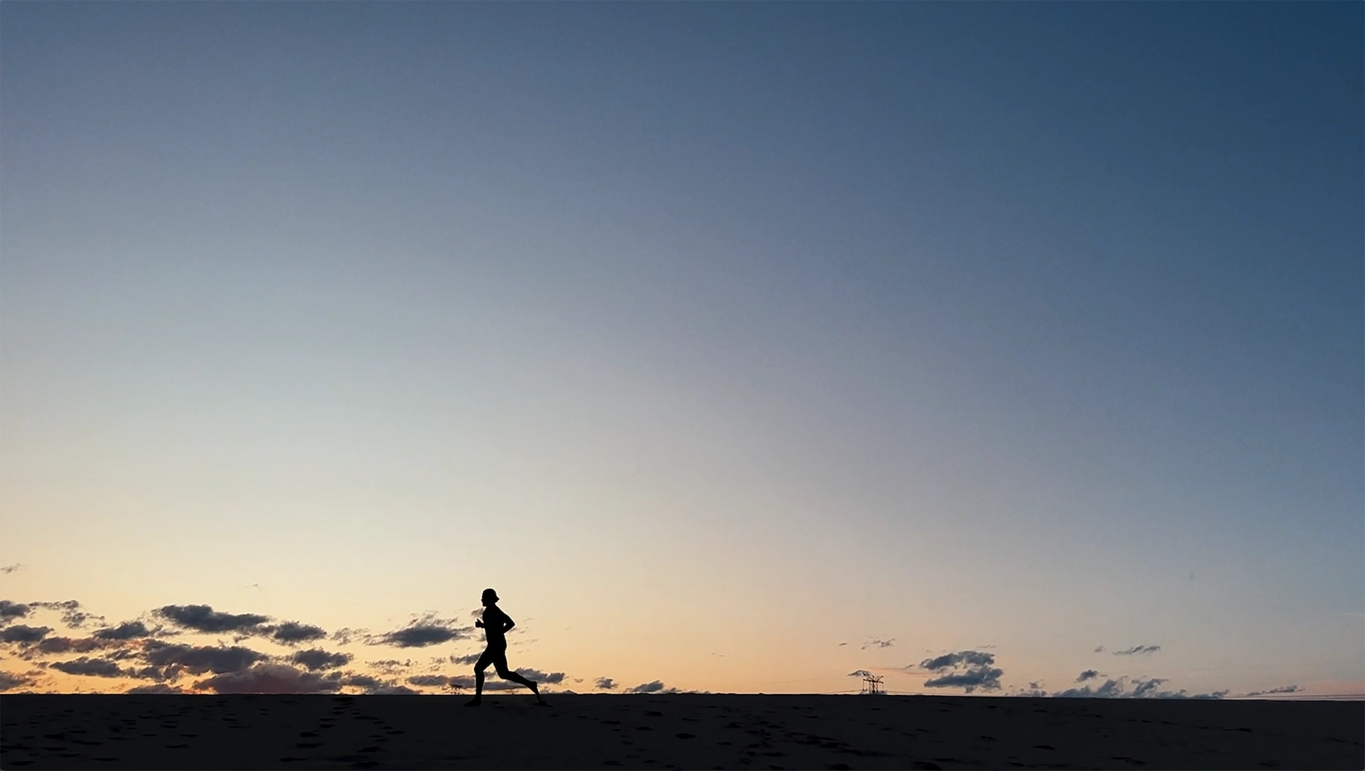 Silhouette of person running at sunrise with orange and blue sky and distant power line structure