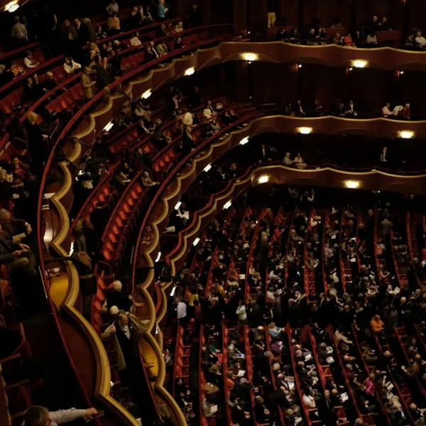 Audience seated in grand theater with ornate balconies and warm lighting during cultural event