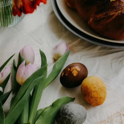 Braided loaf of bread with pastel tulips and decorated Easter eggs on white cloth in spring setting