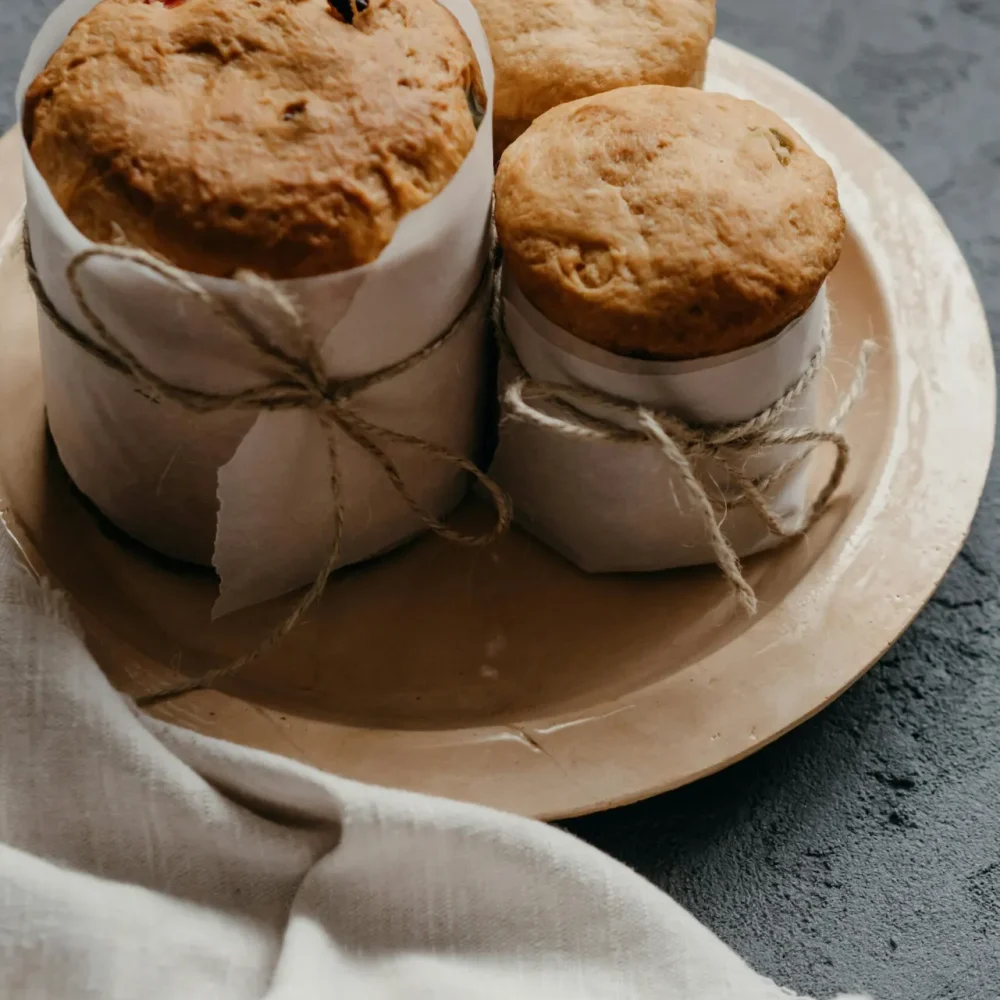 Three artisanal baked goods wrapped in parchment and twine on ceramic plate over dark textured surface