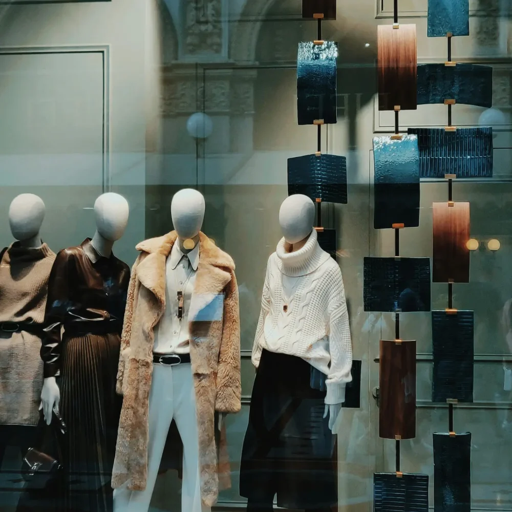 Storefront display with four mannequins in layered winter fashion and neutral tones beside sculptural panels