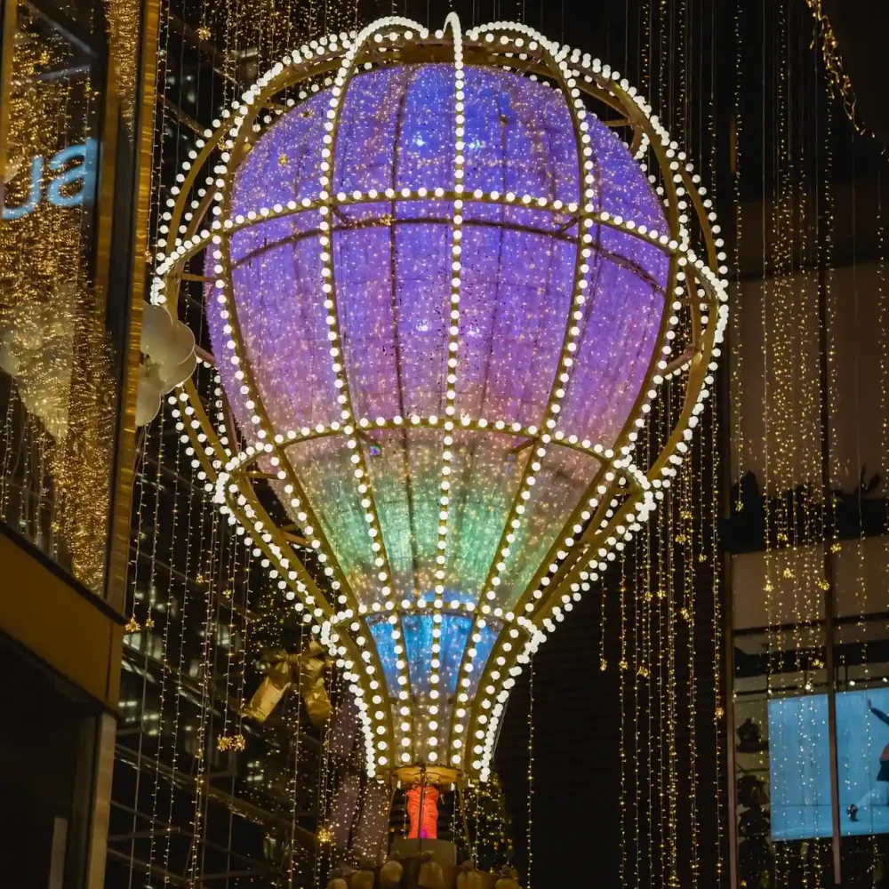 Illuminated hot air balloon installation with gradient lights and golden strings in festive urban setting