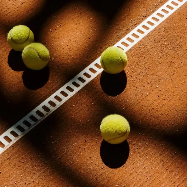 Tennis balls scattered on a clay court under shadows near a white line