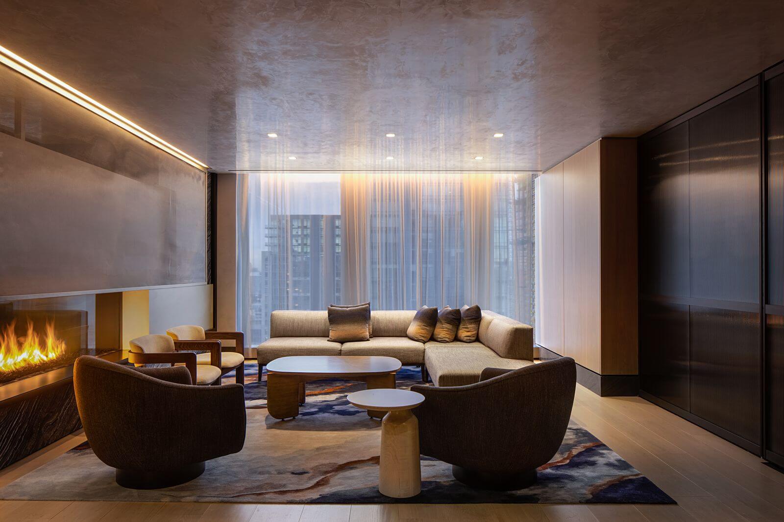 Luxurious living room at Equinox Hotel with beige sectional, fireplace and city view through tall windows