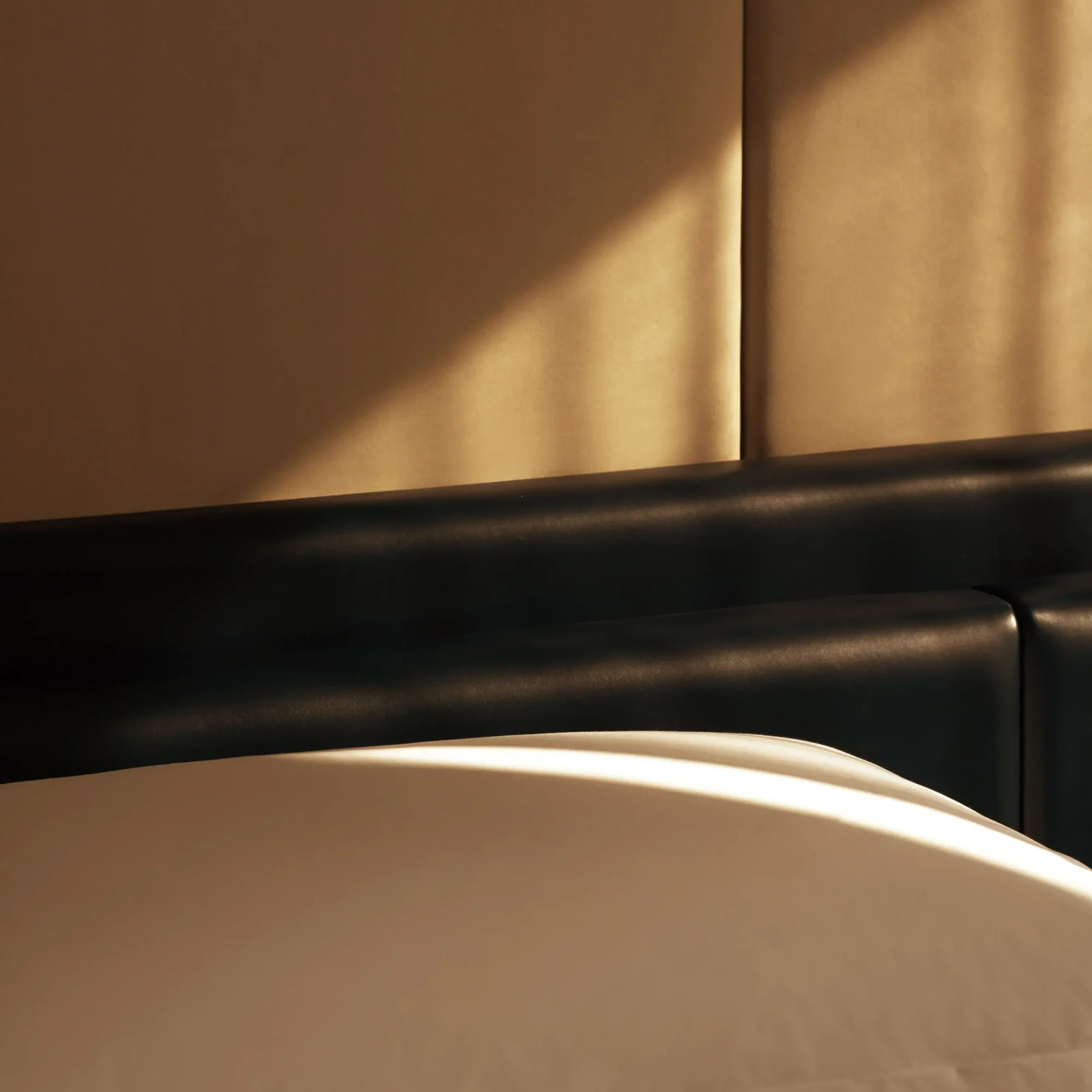 Close-up of bed with white sheets and beige paneled headboard in sunlit Equinox hotel room