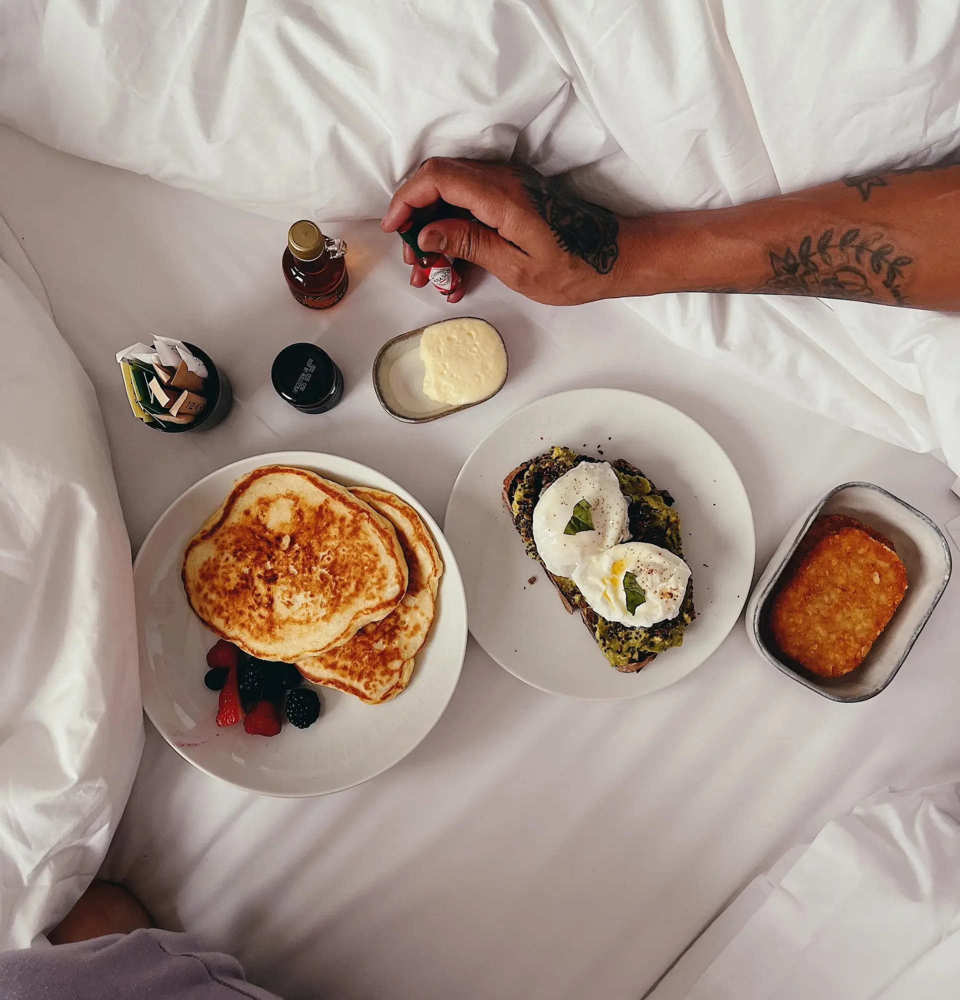 Breakfast in bed at Equinox hotel with pancakes, avocado toast, berries, and hand reaching for jam