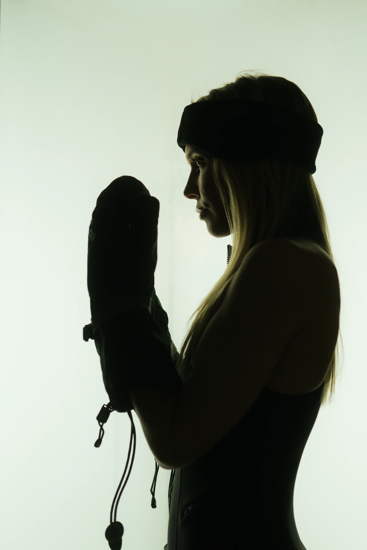 Silhouette of person in headband holding up mittened hands against softly lit background