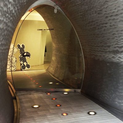 Metallic tunnel entrance to COMME des GARÇONS store with circular floor lights and cartoon figures