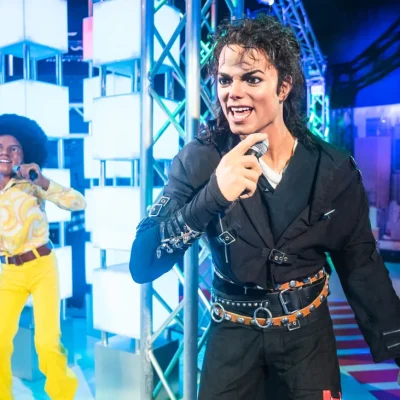Wax figures of Michael Jackson in black buckled outfit and 1970s performer in yellow disco attire on exhibit