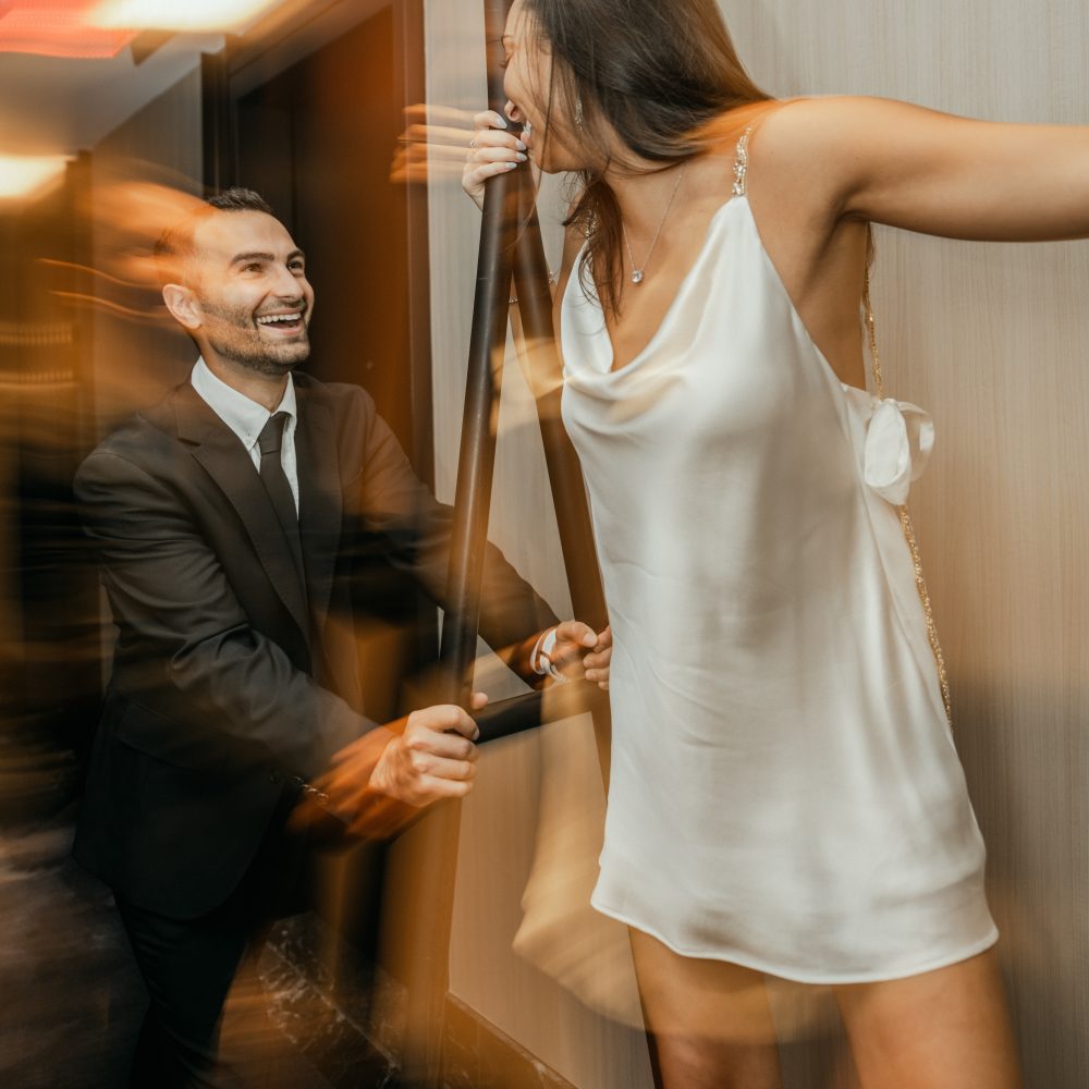 Couple dressed for New Year’s Eve laughing together in a hotel interior