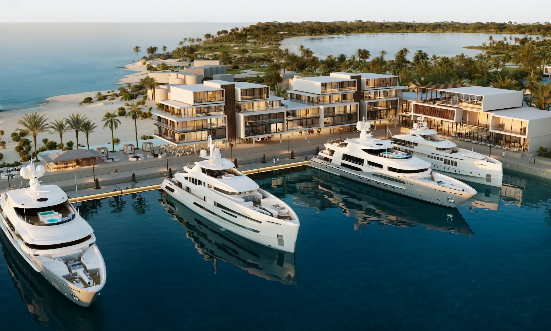 Luxury waterfront resort with white yachts docked at a marina, modern buildings, palm trees, and a curved beach.